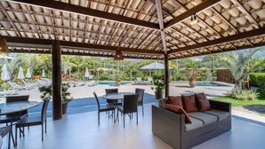 An outdoor patio area with a covered seating area, a pool, and lush greenery.