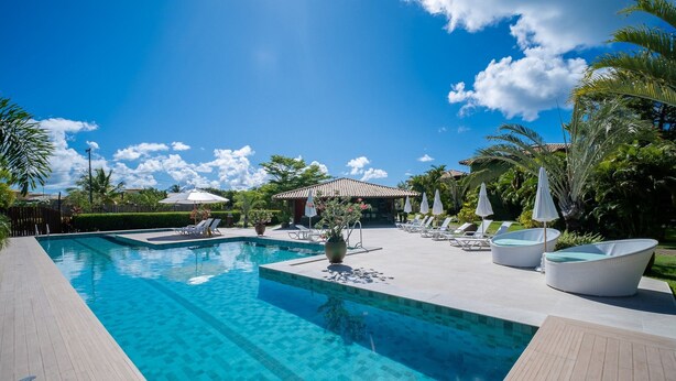 A swimming pool with lounge chairs and umbrellas, surrounded by palm trees and a clear sky.