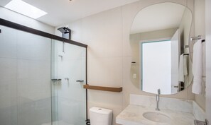 A modern bathroom with a glass shower enclosure, a white toilet, a marble sink, and a large mirror. - NLU - Full-featured Condominium at Marceneiro Beach (Passo de Camaragibe)