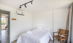 A hotel room with a bed, a wooden chair, a wall-mounted air conditioner, and a sign on the wall. - NLU - Full-featured Condominium at Marceneiro Beach (Passo de Camaragibe)