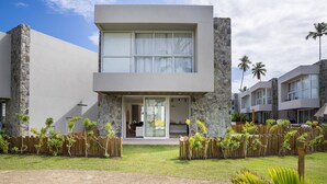 A modern two-story building with stone accents, large windows, and a well-maintained lawn with tropical plants. - NLU - Full-featured Condominium at Marceneiro Beach (Passo de Camaragibe)
