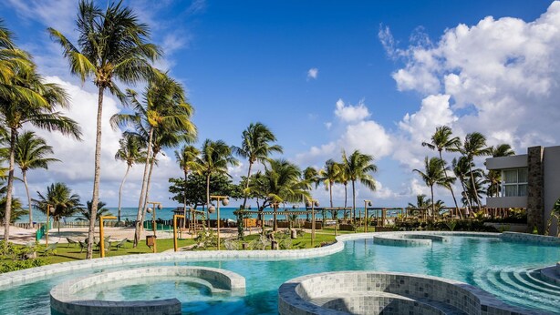 A pool area with palm trees and a view of the ocean. - NLU - Full-featured Condominium at Marceneiro Beach (Passo de Camaragibe)