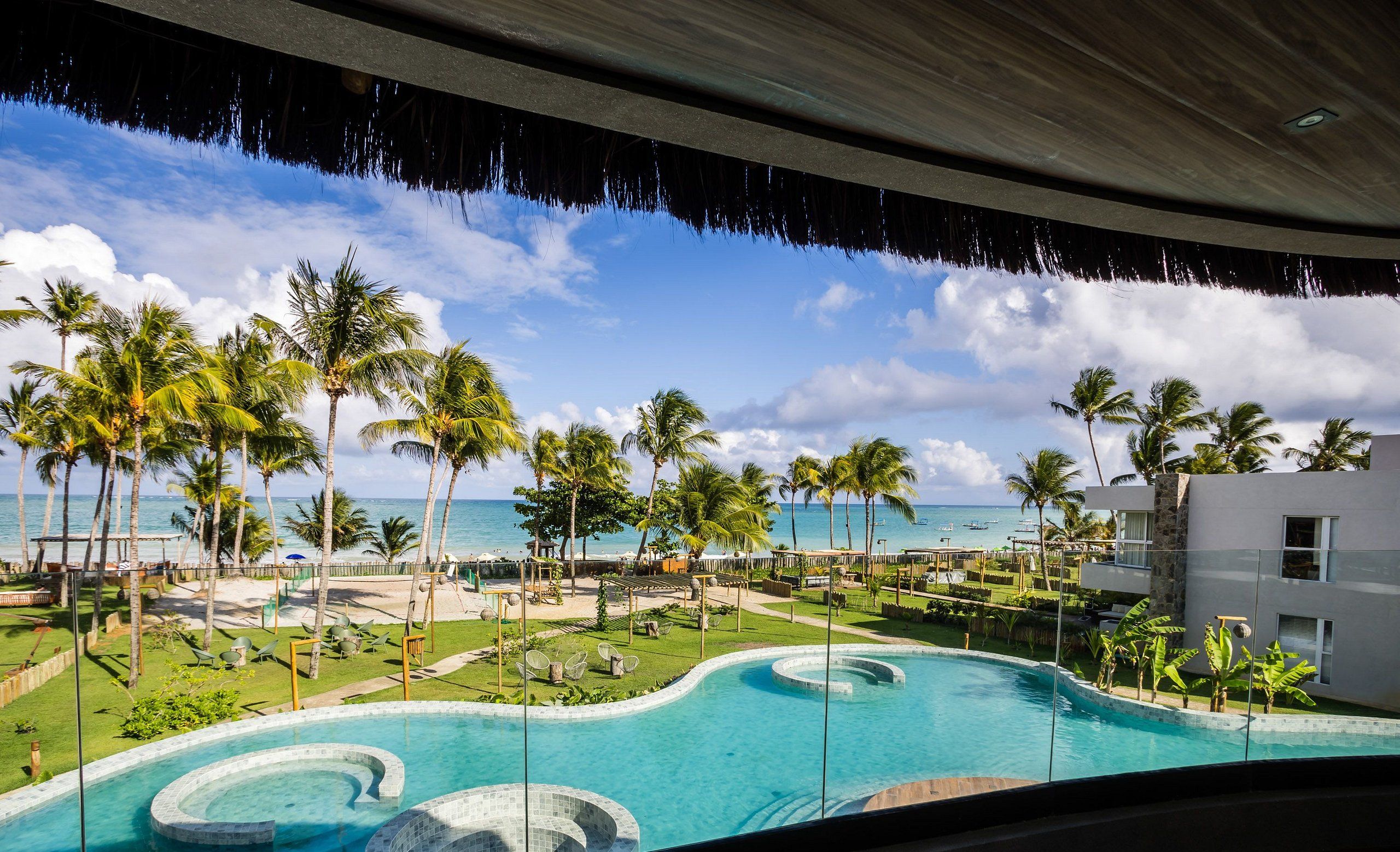 A resort pool with clear blue water, surrounded by palm trees and a view of the ocean.