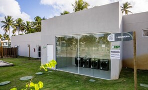 A modern building with a glass facade, a sign for 'LAVANDERIA', and a display of black speakers. - NLU - Full-featured Condominium at Marceneiro Beach (Passo de Camaragibe)