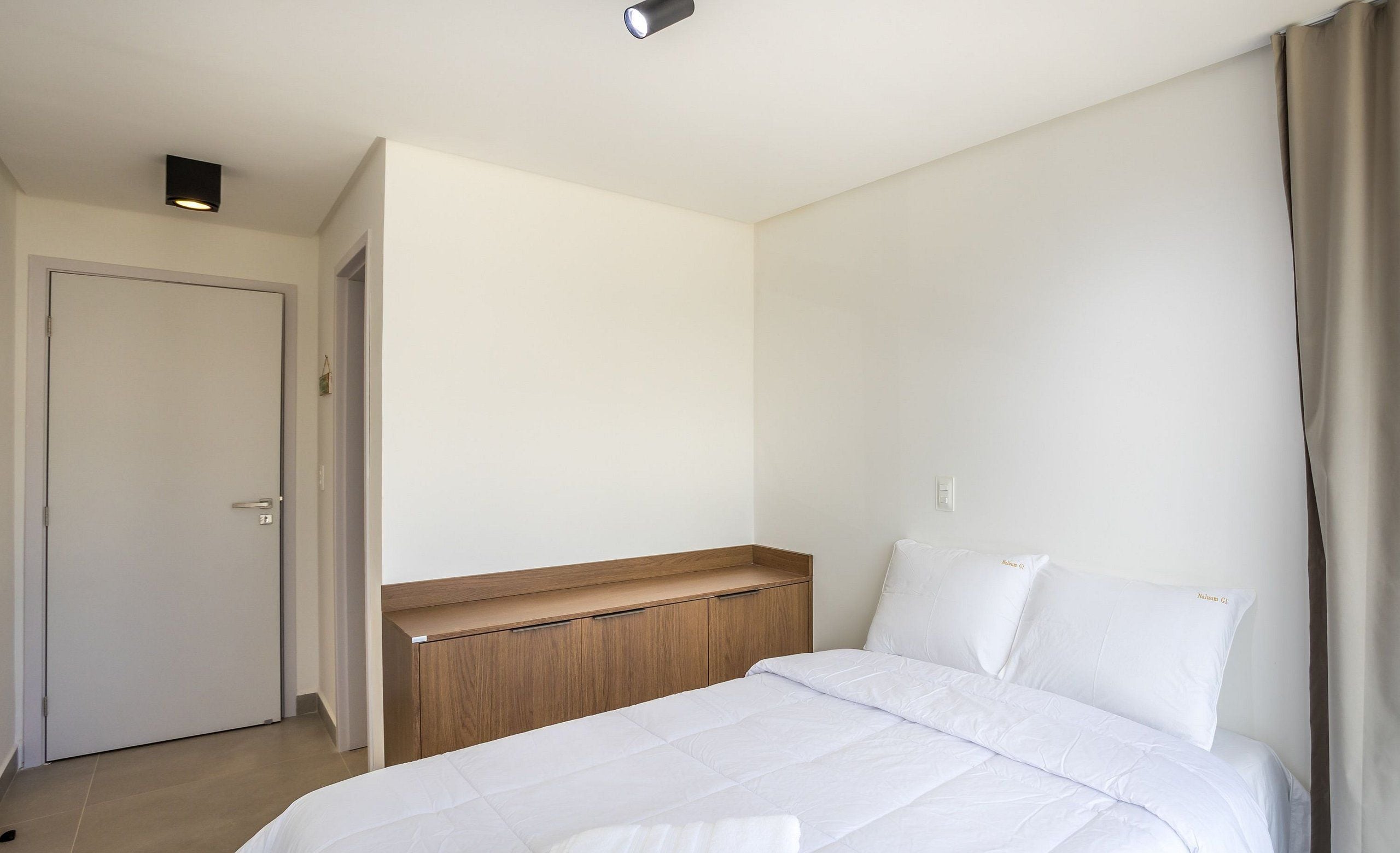 A bedroom with a bed, a wooden headboard, a white door, and a light fixture on the ceiling.