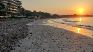A beach with a sunset, pebbles, and a building in the background. - Casitas Las Palmas (Punta de Mita)