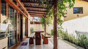 An outdoor patio with a wooden table and benches, surrounded by glass doors and a concrete wall. - House With Pool in the Condominium Cvb0144 (Maraú)