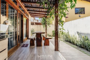 A wooden pergola with a table and benches, a glass door entrance, and a small window with a view of the sky. - House With Pool in the Condominium Cvb0144 (Maraú)