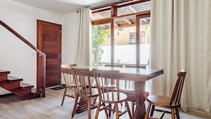 A dining area with a wooden table and chairs, a wooden staircase, and a view through a window with curtains. - House With Pool in the Condominium Cvb0144 (Maraú)