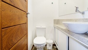 A bathroom with a wooden door, a white toilet, a bidet, and a large sink with a mirror above it.