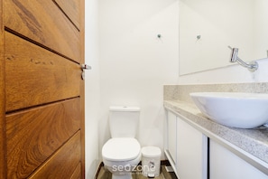 A bathroom with a wooden door, a white toilet, a bidet, and a large sink with a mirror above it. - House With Pool in the Condominium Cvb0144 (Maraú)