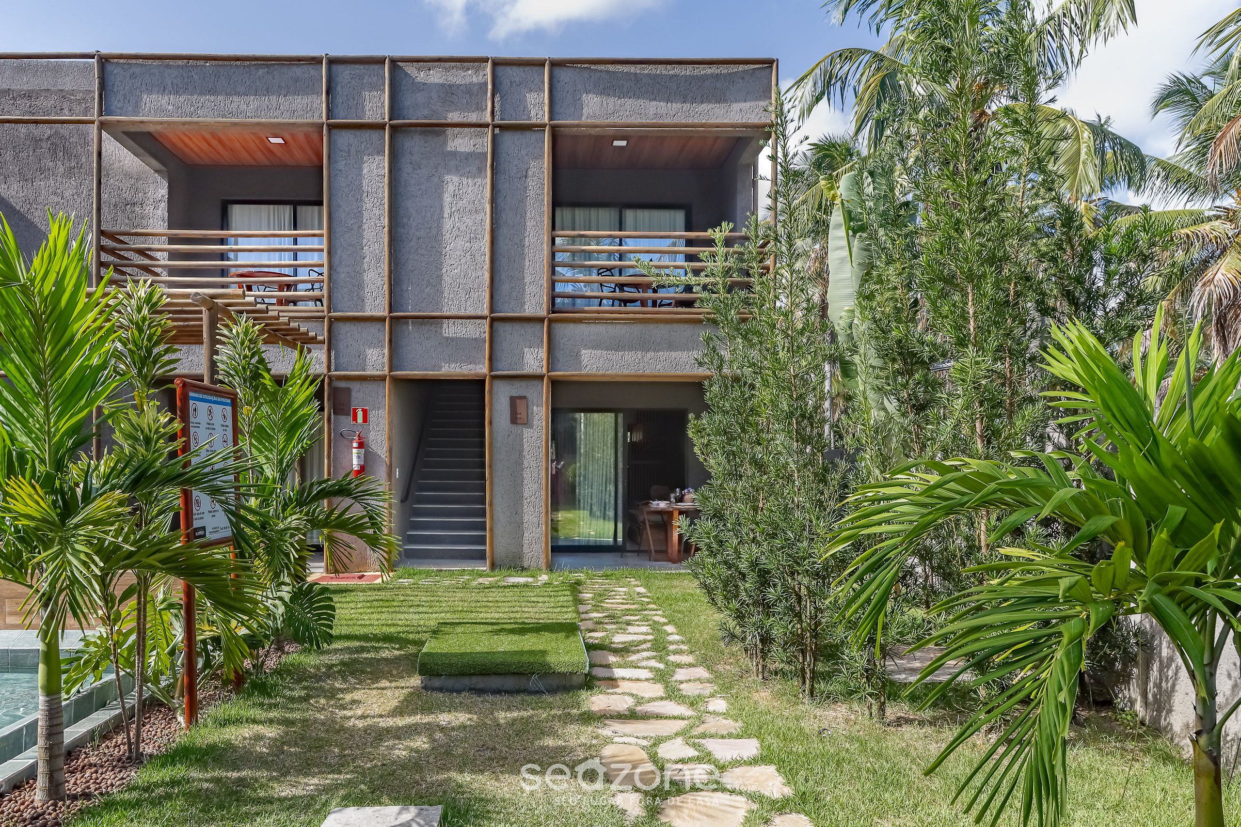Een modern gebouw met twee verdiepingen, een balkon, een pad van natuursteen en tropische planten.