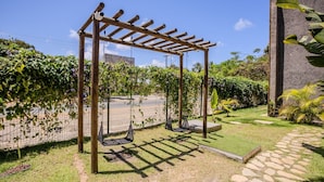 Un jardín con un porche de madera, dos columpios y un sendero de piedra.