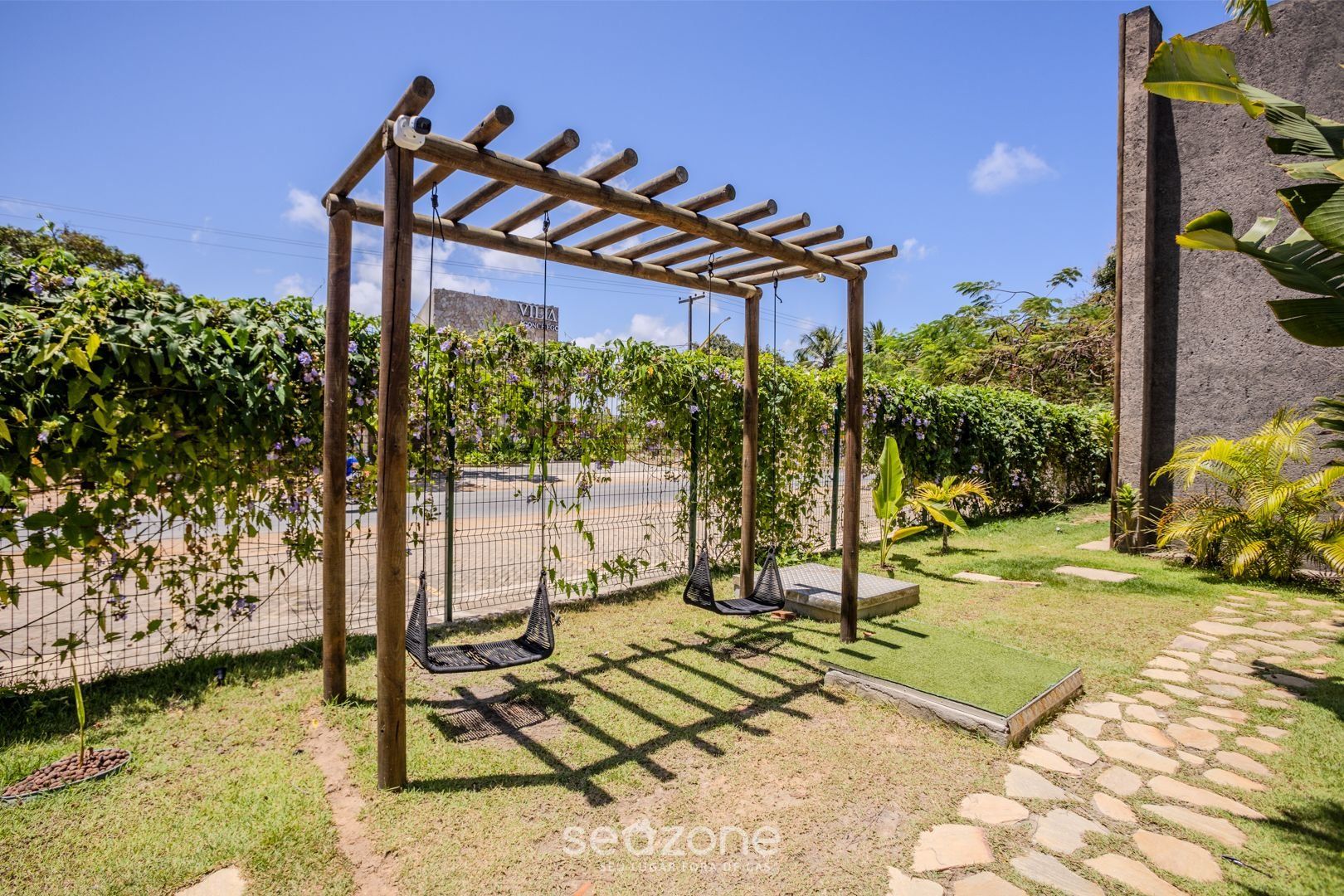 Un giardino con una pergola in legno, due altalene e un viale lastricato in pietra.