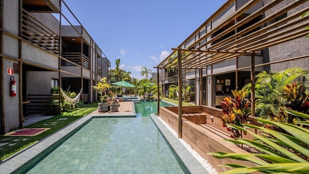 Un área de piscina moderna con piscina cristalina, terraza de madera y plantas tropicales.