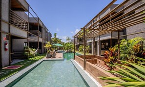 Un espace piscine moderne avec une piscine à eau claire, une terrasse en bois et des plantes tropicales.