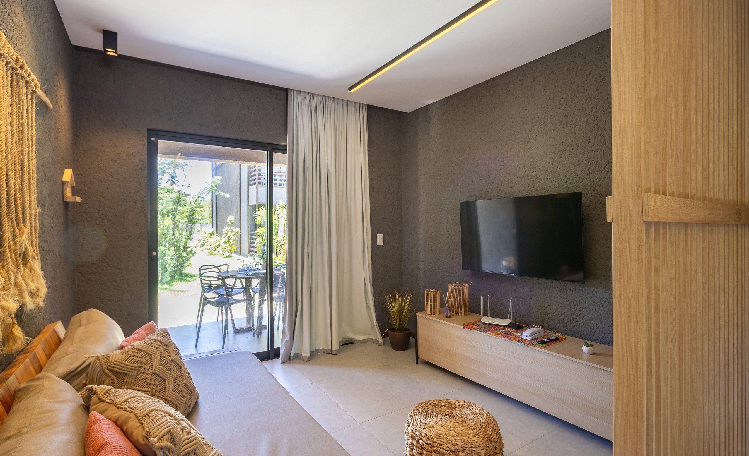Un salon moderne avec un canapé, un téléviseur fixé au mur, un meuble en bois et une grande fenêtre avec des rideaux.