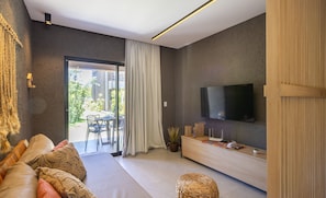 Un salon moderne avec un canapé, un téléviseur fixé au mur, un meuble en bois et une grande fenêtre avec des rideaux.