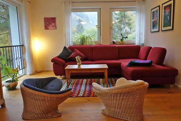 Una sala de estar con un sofá rojo, dos sillones de mimbre, una mesa de centro de madera y una alfombra colorida.