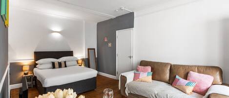 A modern hotel room with a bed, a sofa, a dining table with tulips, and a wine glass.