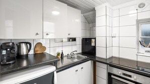 Uma cozinha moderna com armários brancos, bancada preta, uma cafeteira Bosch, chaleira e tábua de corte de madeira.