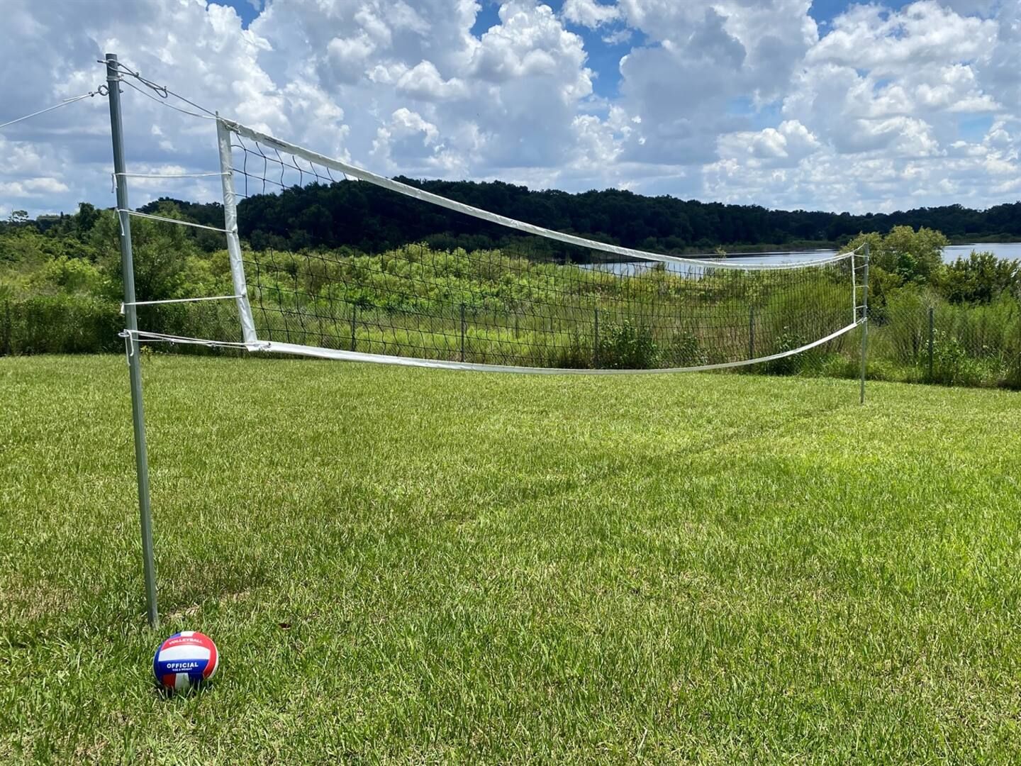 Een volleybalnet opgesteld in een grasveld, met een heldere lucht en bomen op de achtergrond.