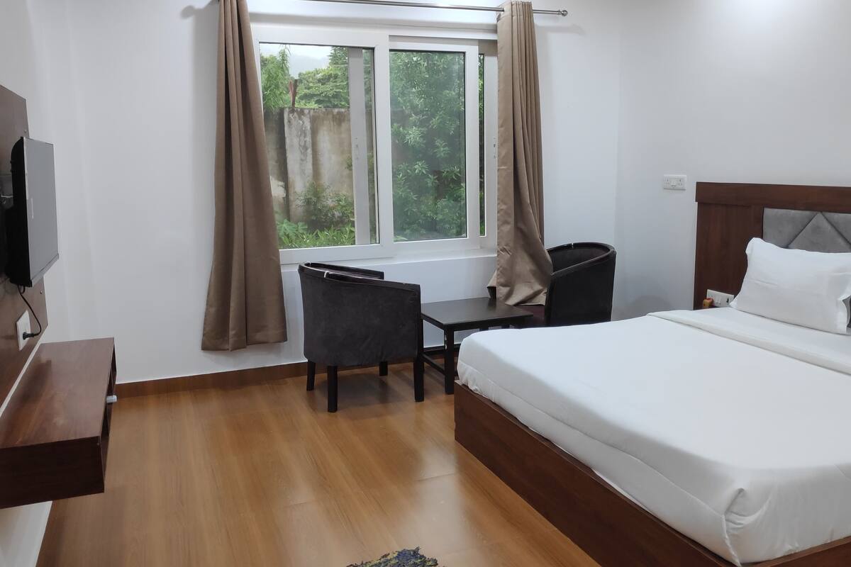 Ein Hotelzimmer mit Bett, Schreibtisch mit Stuhl, Wandfernseher und einem Vorhangfenster.