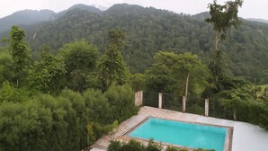 A pool surrounded by lush greenery and mountains in the background. - Dreamland Resort (Kaladhungi)