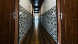 A long, narrow hallway with wooden doors on both sides and a brick wall on the left. - Dreamland Resort (Kaladhungi)