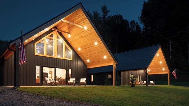 Une cabane moderne dotée d’un grand porche à l’avant, de grandes fenêtres et d’un drapeau américain.