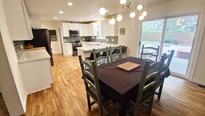 A modern kitchen with white cabinets, a central island, and a dining area with a table and chairs. - Forest Retreat at Canyon Loop (Flagstaff)