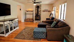 A living room with a sofa, ottoman, TV, fireplace, and wooden floors. - Forest Retreat at Canyon Loop (Flagstaff)