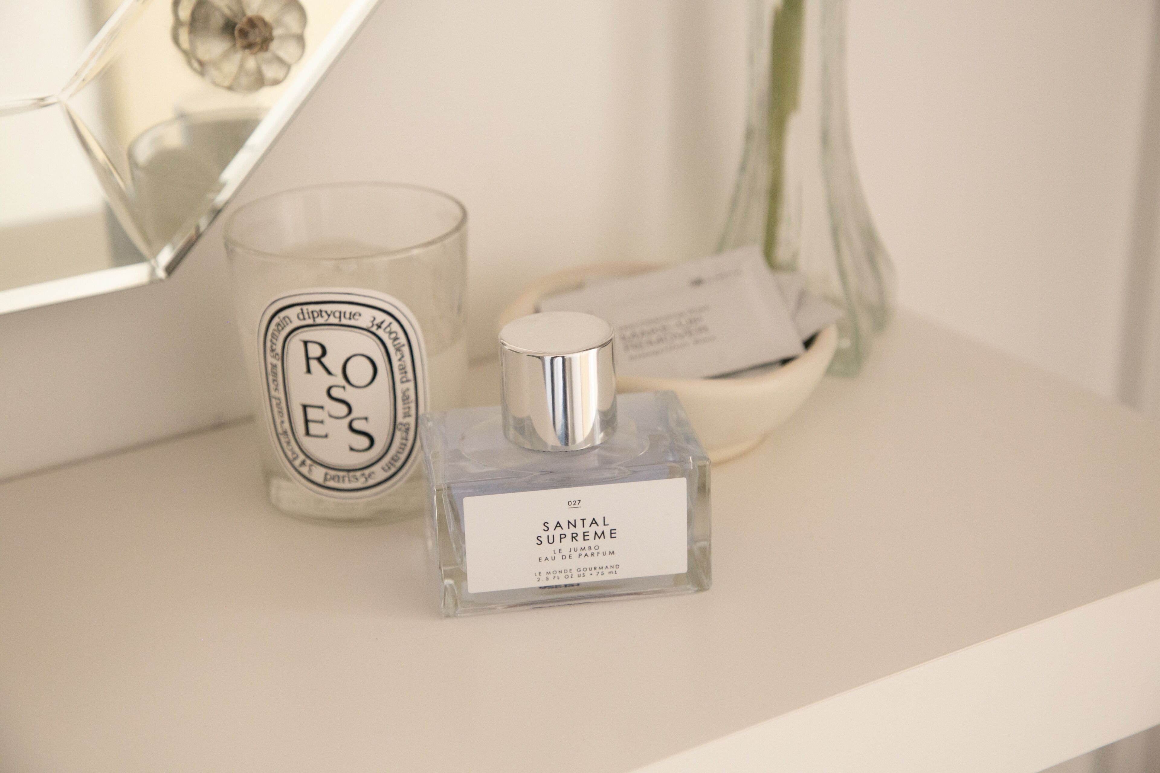 A bathroom with a mirror, a glass candle, and a bottle of Santal Supreme cologne.