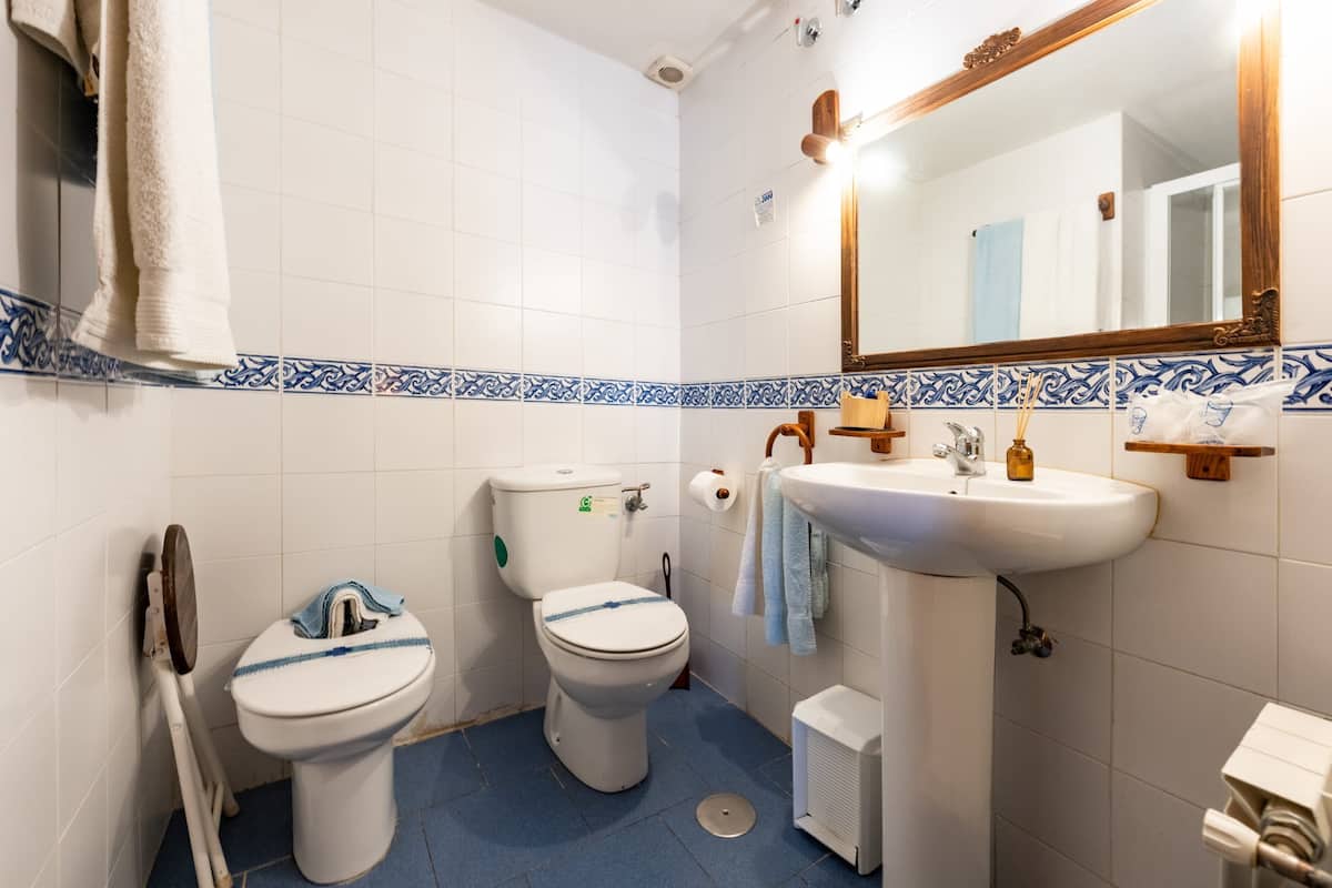 Une salle de bain avec deux toilettes, un lavabo, un miroir et un sol carrelé de carreaux bleus.