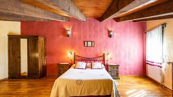 Un dormitorio con techo de madera, una cama con edredón blanco, dos mesitas de noche, un armario de madera y una ventana con cortinas.