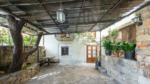 A stone courtyard with a rustic wooden bench, a hanging lantern, and potted plants.