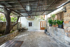Un patio de piedra con un banco de madera rústica, un farol colgante y plantas en macetas.