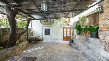 Un patio de piedra con un banco de madera rústica, un farol colgante y plantas en macetas.