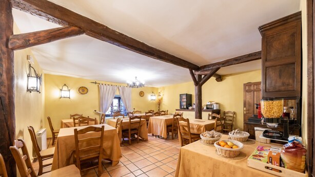 A dining area with wooden tables and chairs, a kitchen area with a bread machine, and a tiled floor.