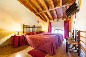 Une chambre avec deux lits, des poutres en bois au plafond, un téléviseur fixé au mur et une chaise.