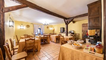 Un comedor con mesas y sillas de madera, una zona de cocina con una máquina para pan y un suelo de baldosas.