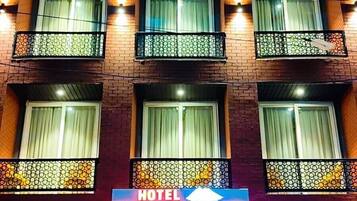 Un hotel de varios pisos con balcones, un letrero que dice "HOTEL GANGA AAMANTARAN" y una zona de recepción con un mostrador y sillas.