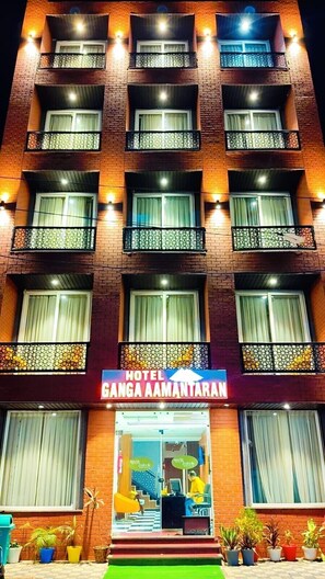 Un hotel a più piani con balconi, un cartello con su scritto "HOTEL GANGA AAMANTARAN" e una reception con scrivania e sedie.