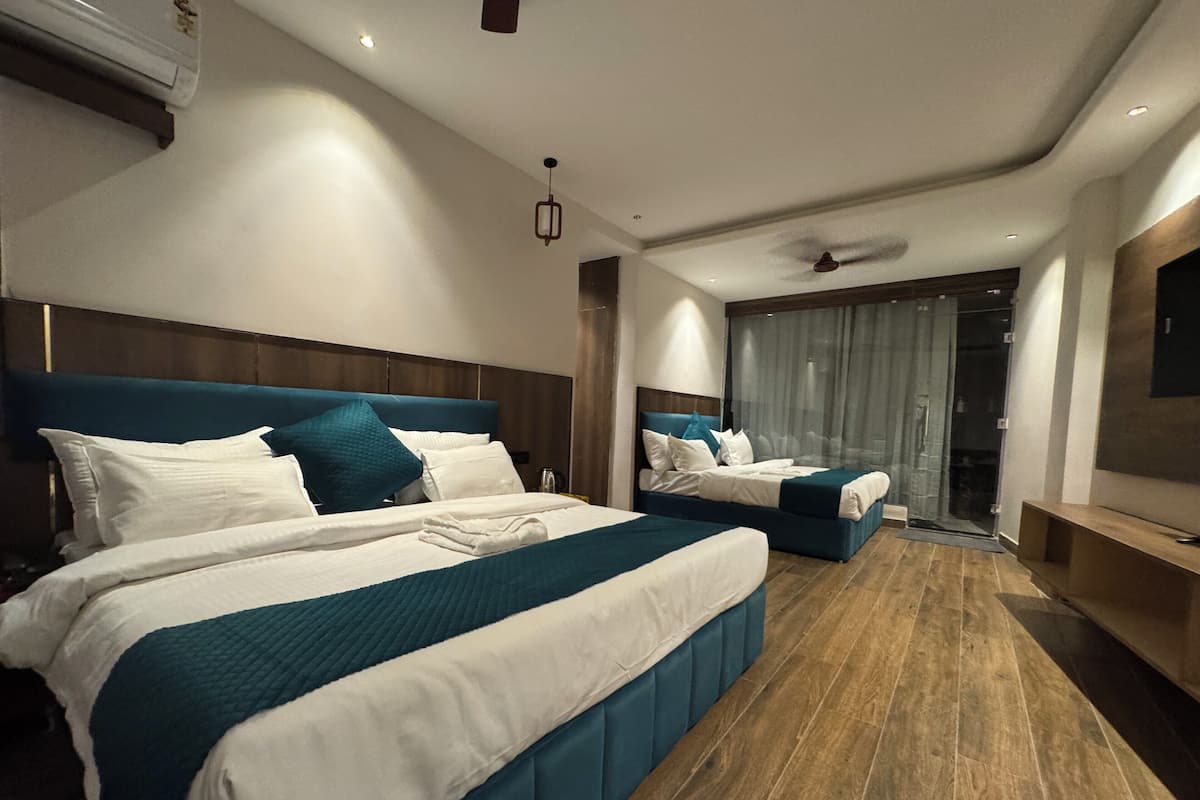 Habitació d'hotel moderna amb dos llits, una finestra gran amb cortines, un ventilador de sostre i una televisió de pantalla plana.