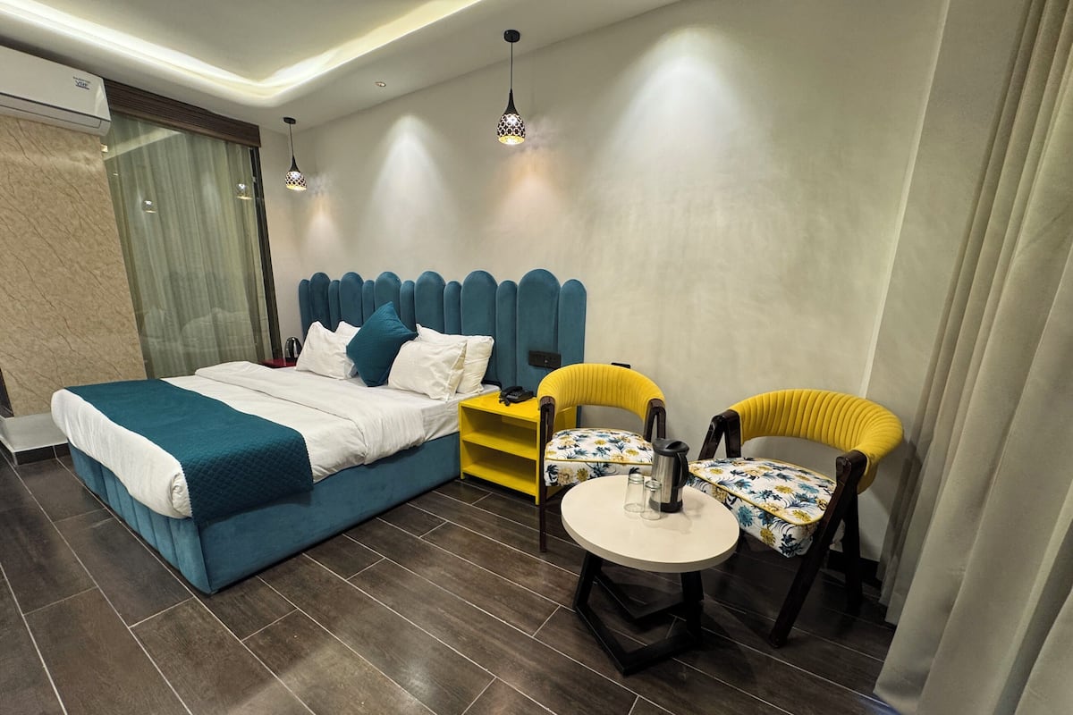 Habitació d'hotel moderna amb un llit gran, una taula petita amb cadires i una taula de nit amb un telèfon i una paperera.