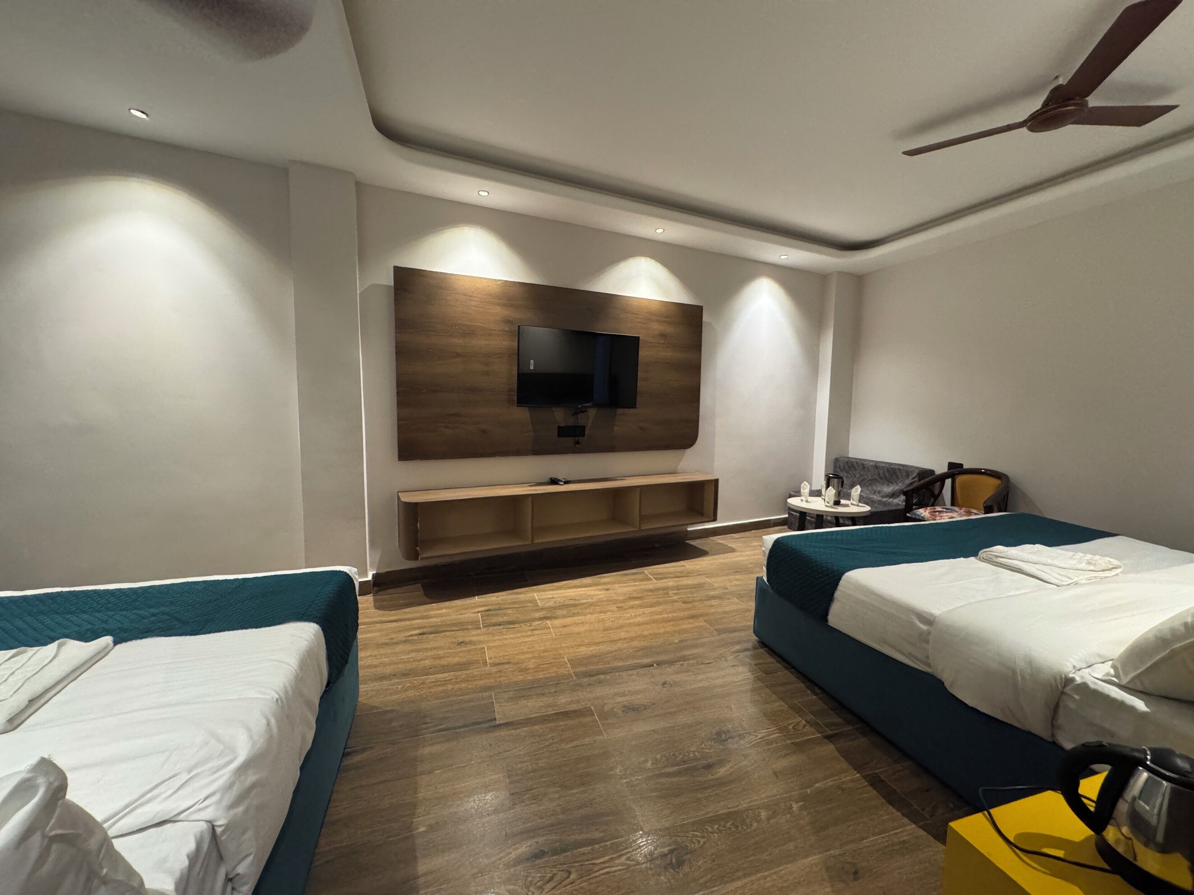 Habitació d'hotel amb dos llits, un televisor fixat a un panell de fusta, una taula petita amb una cadira i un ventilador de sostre.
