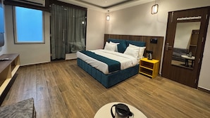 A modern bedroom with a large bed, a ceiling fan, a window, and a bathroom mirror. - Hotel Ganga Aamantran (Haridwar)