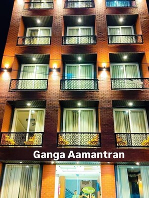 Un immeuble à plusieurs étages doté de balcons, une enseigne indiquant « Ganga Aamran » et une entrée bien éclairée.