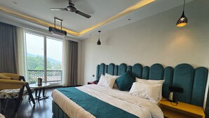 A hotel room with a large bed, a chair, a small table, and a view of the outdoors. - Hotel Ganga Aamantran (Haridwar)