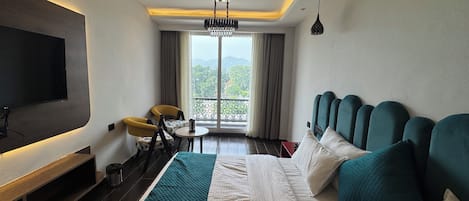 Une chambre d’hôtel comprenant un lit, une télévision, un ventilateur de plafond, un lustre, un balcon avec vue et une table avec des chaises.